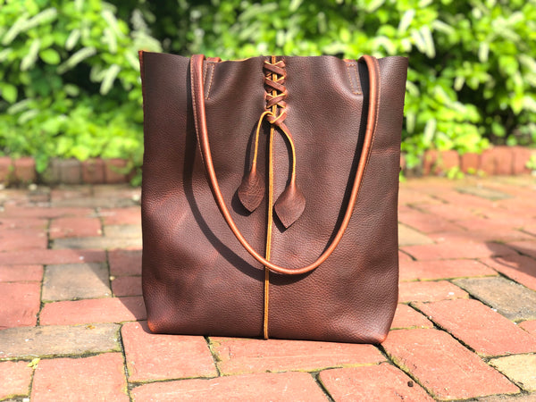 Tall brown leather tote with middle stitch and leaf tassels